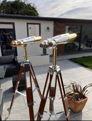 WW2 Binoculars - Aviation and Binoculars Two brass telescopes mounted on wooden tripods on a patio in a backyard.